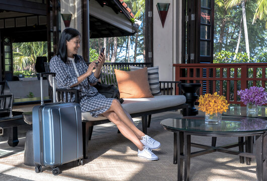 Asian woman tourist using smartphone and sitting in hotel lobby, Holiday vacation concept