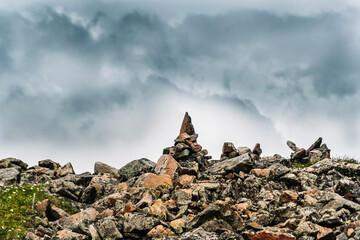 Stone pyramids of cobblestones on top of mountain under thick clouds overlooking valley. Landmark for navigating in fog in highlands. Meditation to strengthen strength of spirit.