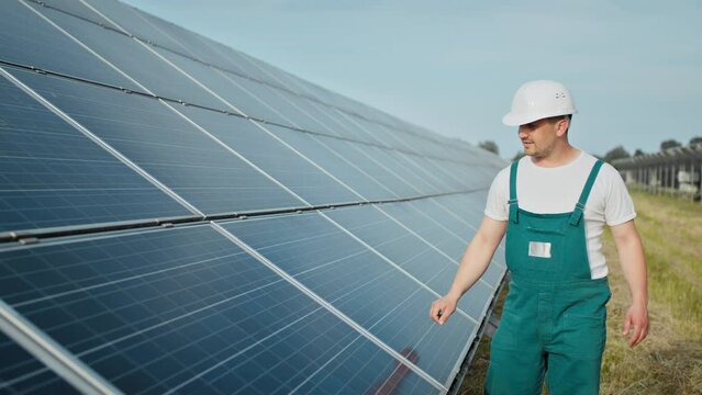 Engineer is checking the operation of sun and cleanliness of photovoltaic solar panels. Concept renewable energy. Caucasian man in hard helmet examining object solar panels. Concept of green energy.