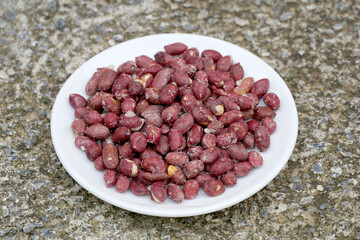 roasted salty peanuts in a white plate on concrete background.