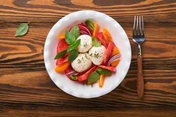 Caprese salad. Italian caprese salad with sliced tomatoes, mozzarella cheese, basil, olive oil in white plate over old wooden brawn background. Delicious Italian food. Top view. Rustic style.