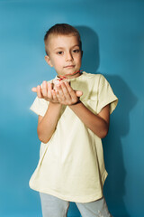 A 6-7-year-old boy in a yellow T-shirt holds little gift in the hands on a blue background. Close-up portrait, front view