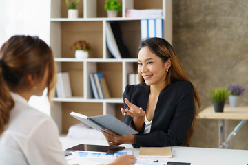 Two Asian business women talk, consult, plan work on the presentation of a new start-up project idea analysis of marketing plans and investments in the office.