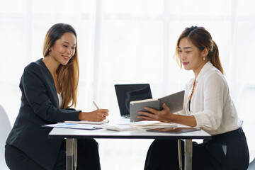 Two Asian business women talk, consult, plan work on the presentation of a new start-up project idea analysis of marketing plans and investments in the office.