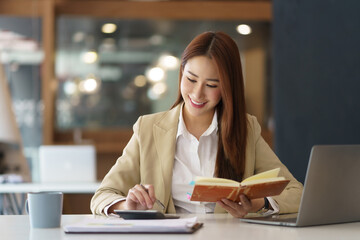 Beautiful Asian businesswoman working on paperwork at her desk in the office review work from different department, take minute of meetings report other document.