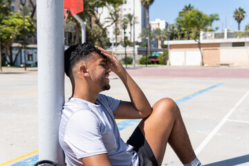 Portrait of a young muslim basketball player smiling and resting on a city court, urban sport concept