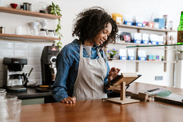 Young black female barista standing by paying terminal in cafe