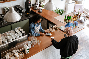 Young black female barista standing by counter with customer in cafe