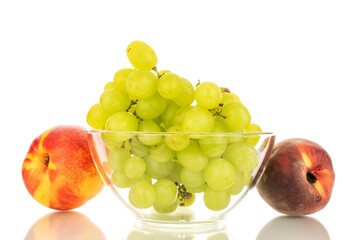 One bunch of white grapes in a glass bowl, next to a peach and a nectarine, close-up isolated on a white background.