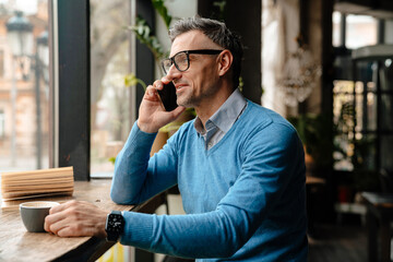 Adult business man in glasses and blue sweater talking phone