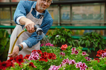 White man watering plants with garden hose while working in greenhouse