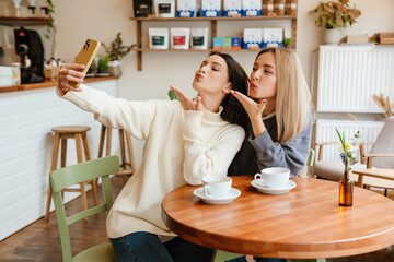 White women gesturing and taking selfie on cellphone in cafe