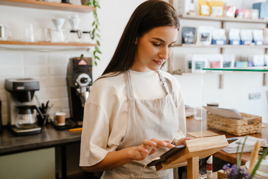 White barista woman wearing apron working with tablet computer in cafe