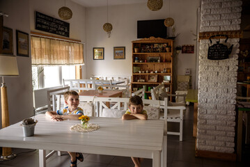 Modern cafe interior style, eco environmental with plant on wall, coffee shop. Two children sitting on bench near table waiting for tasty meal