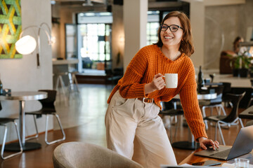 White ginger woman drinking coffee while working with laptop at office