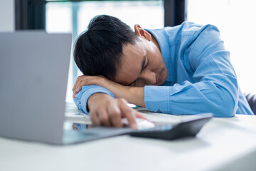 Tired businessman sleeping in the office. Asian business man  worked late and fell asleep on the computer keyboard. Tired male worker resting in office.