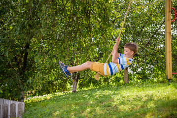 Two adorable happy little boys is having fun on a rope swing which he has found while having rest...