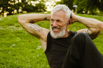 Mature gray sportsman wearing earphones doing workout in park