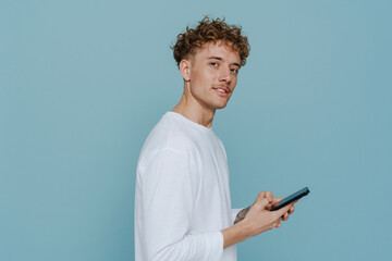 Young handsome curly man holding phone and looking at camera