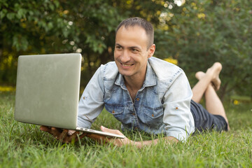 Obraz premium Young man in the garden in summer on the laptop computer while chatting online as a freelancer.