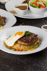 Grilled beef steaks with potato, vegie and steak sauce at white plate on texture rustic table