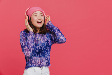Young cute asian girl in pink winter hat touching headphones