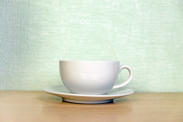 White coffee or tea cup with a saucer on a wooden table against the wall. Place for text