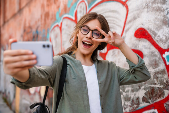 Young beautiful smiling woman taking selfie and showing victory gesture