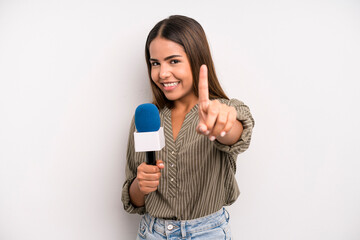 hispanic pretty woman smiling proudly and confidently making number one. presenter with a...