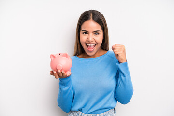 hispanic pretty woman feeling shocked,laughing and celebrating success. piggy bank concept