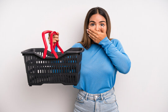 hispanic pretty woman covering mouth with hands with a shocked. empty supermarket basket concept