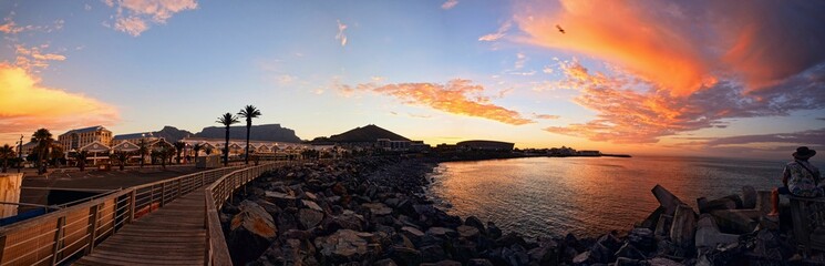 Panoramic shot of a wooden walkway by a rocky coast at sunset in Cape Town, South Africa