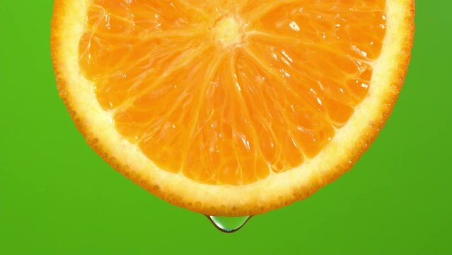 Water drop falling from orange hue orange on green background. Orange slice and water splashing, drops of juice falling from juicy fruit. Making cocktail of fruits, drinking cold lemonade