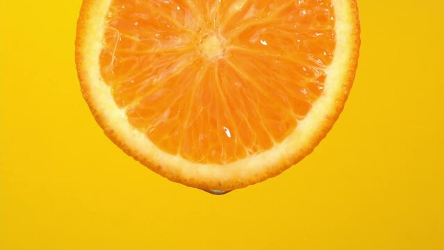 Natural oil drop falling from orange on yellow background. Orange slice and water splashing, drops of juice falling from juicy fruit. Making cocktail of fruits, drinking cold lemonade