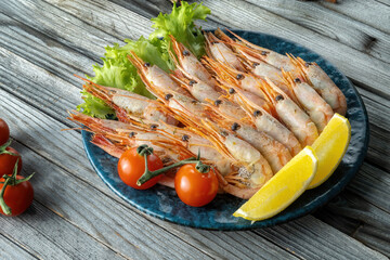 Boiled shrimps on a wooden background, lemon and tomatoes. Macro