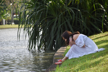 woman sitting by the river looking at fish At the outdoor park, close to nature, there is a big river.