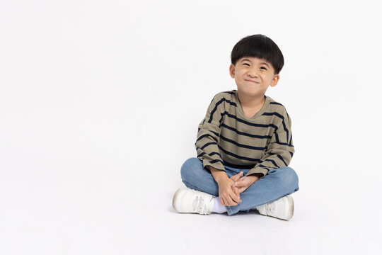 Happy Asian little boy smiling and sitting on floor isolated on white background, Full body composition and five years old