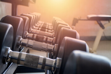 Close-up shot of dumbbells set on a shelf inside an empty workout gym against a backdrop of light from a window.