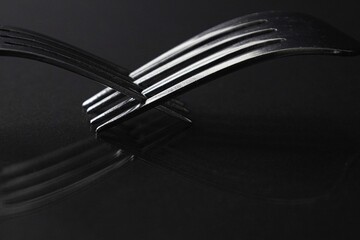 Two silver forks with crossed tines on black reflective surface