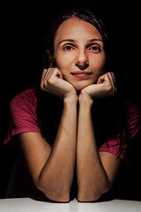 beautiful woman is prop up chin and look in camera. Low key portrait. Brunette propping her chin with her hands