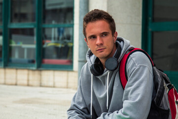 young student boy sitting with backpack and books and wearing headphones