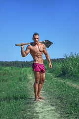 Strong muscular sexy wet young handsome dirty guy with athletic body in red underwear posing with shovel outdoors. Fitness male model posing with shovel
