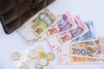 Croatian kunas and coins of different denominations on a white background near a black handbag.