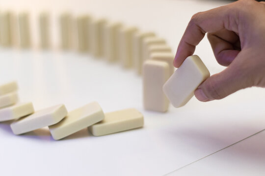 White brick dominoes on top of bright base and background, hand removing single domino.