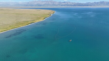 Drone view of a boat in the sea with a grass field and mountains in the background
