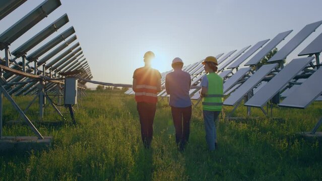 Concept of renewable energy and ecological innovation walking at sunset group of ecological engineers and assistant they analysing the cleanliness of photovoltaic solar panels and operation of sun