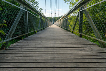 Fototapeta premium An old wooden suspension bridge over the river in the park. Wooden background for text. Autumn landscape.