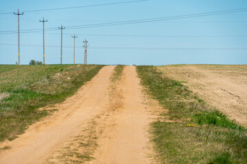 A dry sandy road passes through a field under the scorching sun and clouds. Dirt road outside the city in the village. Arid climate on earth. Climate change and its consequences.