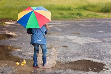 Child holding a colorful umbrella jumping into the rain puddle with bathroom ducks