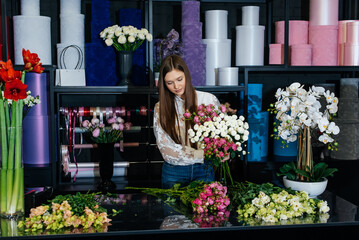 A young female florist takes care of flowers in a cozy flower shop and collects bouquets. Floristry and making of buckets in a flower shop. Small business.